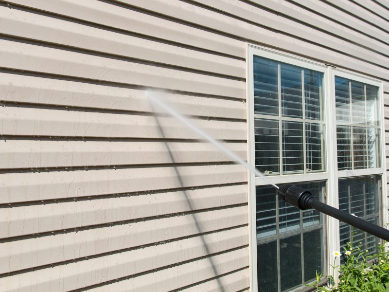 Power washing. House wall vinyl siding cleaning with high pressure water jet.